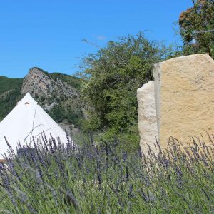 Tente safari au milieu de champs de lavande, avec montagnes en arrière-plan.