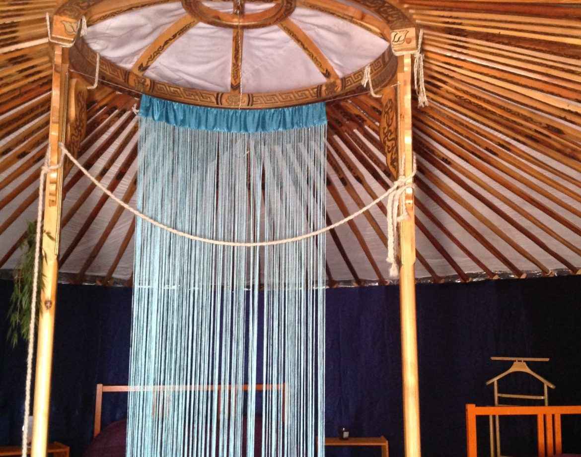 Yourte spacieuse avec un plafond en bois sculpté et des lits confortables.