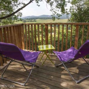 Cabane perchée en Midi-Pyrénées avec chaises violettes et vue sur la vallée.