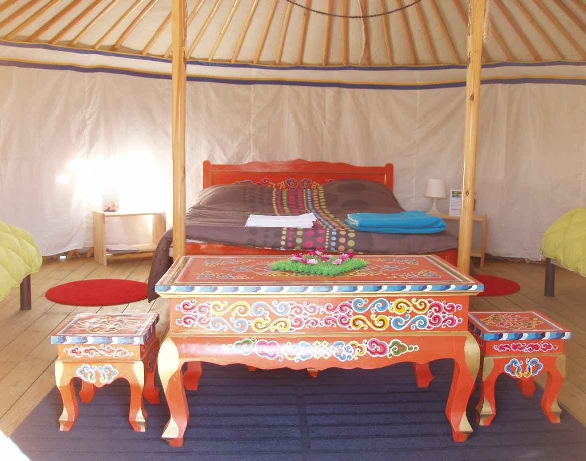 Yourte colorée avec un lit douillet et des meubles décoratifs en bois.