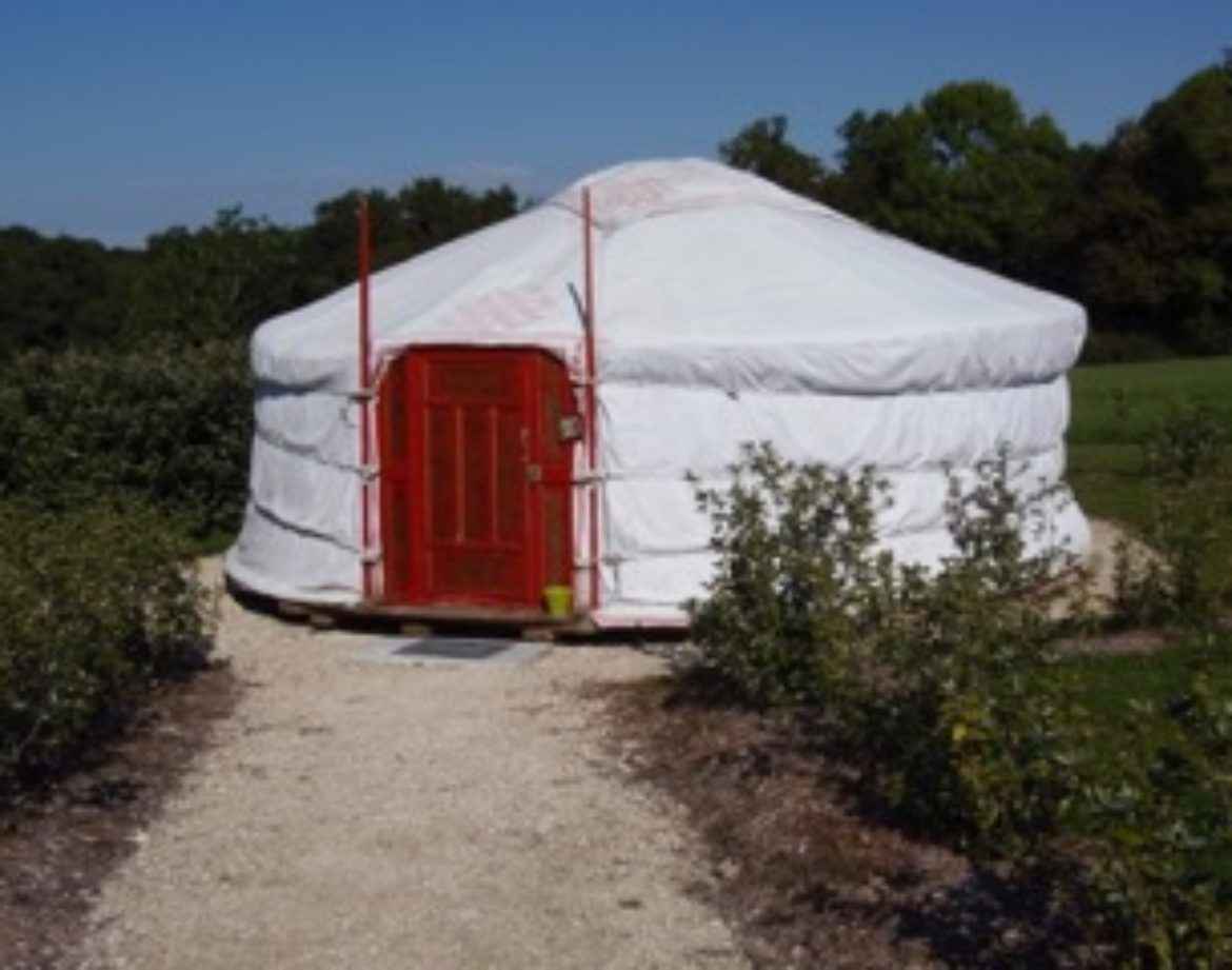 Yourte blanche avec porte rouge, entourée de verdure au Centre de la France.
