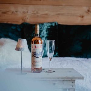 Hébergement insolite en bois avec bouteille de Lillet et verre sur table.