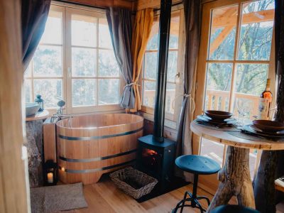 Cabane en bois avec baignoire en bois et poêle à bois, vue sur la nature.