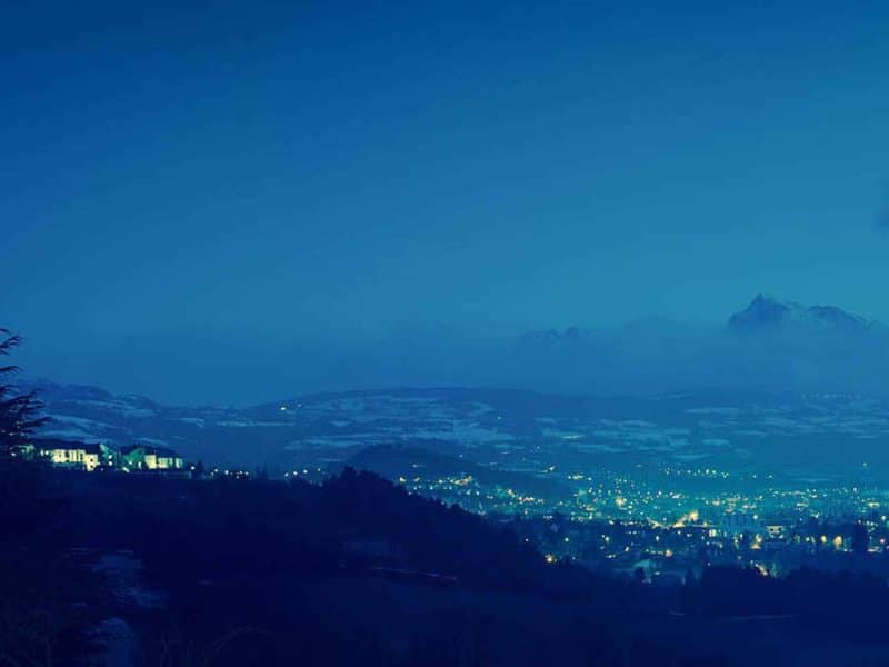 Hébergement en chalet avec vue nocturne sur la vallée illuminée et les montagnes.