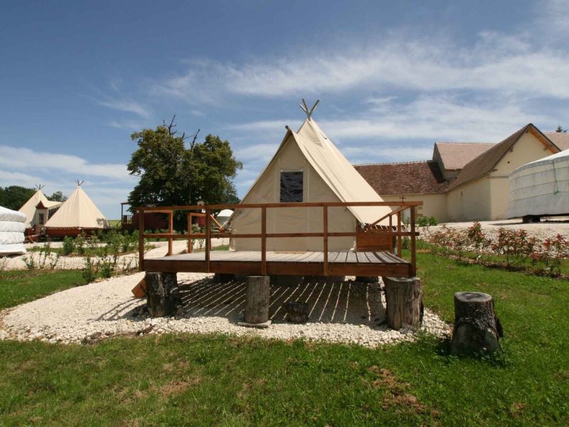 Tentes en toile sur plateforme en bois, entourées de verdure et de ciel bleu.