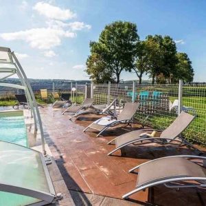 Hébergement insolite en Auvergne avec piscine et chaises longues au bord dun paysage verdoyant.