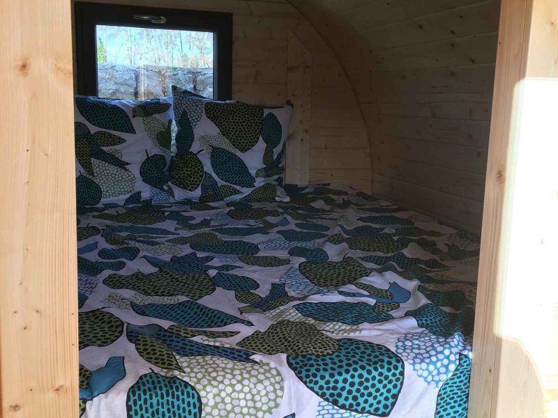 Cabane en bois avec lit douillet, draps à motifs colorés et ambiance chaleureuse.