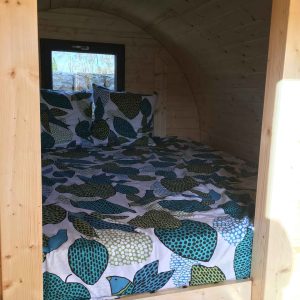 Cabane en bois avec lit douillet, draps à motifs colorés et ambiance chaleureuse.