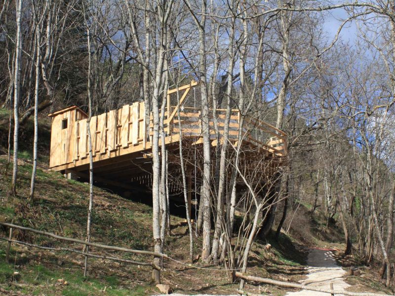 Cabane en bois sur pilotis, entourée darbres, offrant un cadre naturel apaisant.