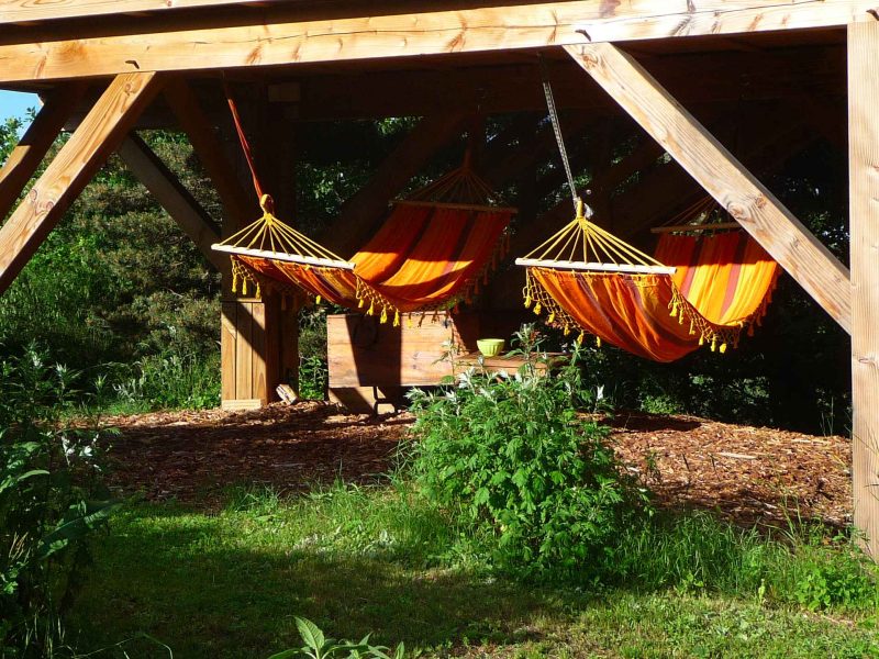 Hébergement en plein air avec hamacs orange suspendus sous une structure en bois.