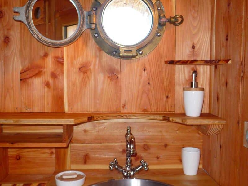 Salle de bain en bois avec lavabo en inox et miroir rond en métal.