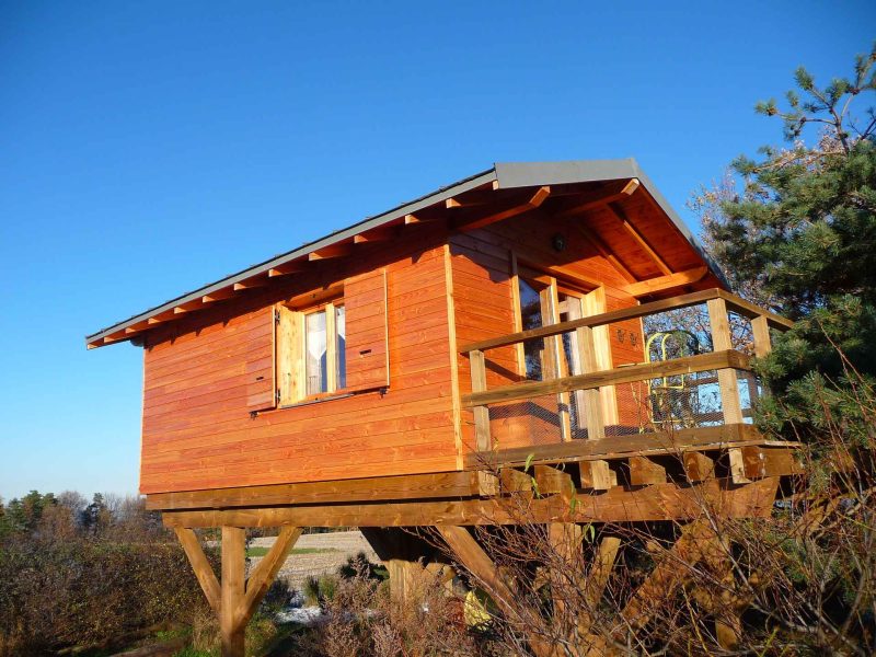Cabane en bois sur pilotis, avec balustrade et vue dégagée sur la nature.