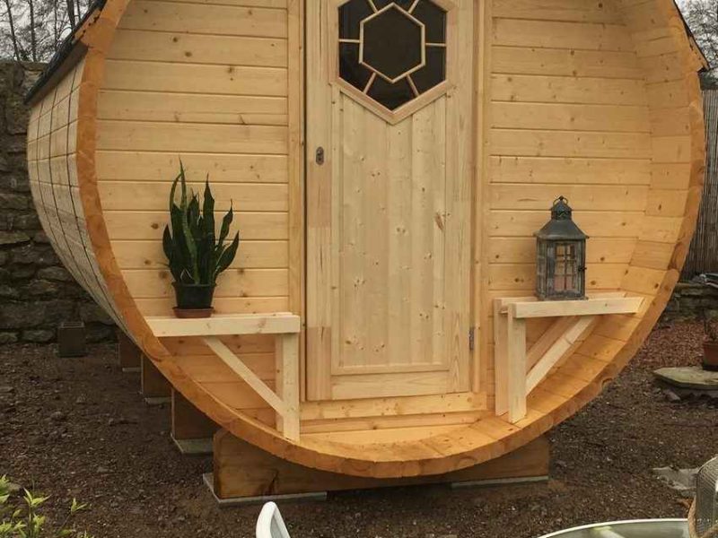 Cabane en bois en forme de tonneau avec une porte en bois et une plante décorative.