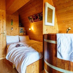 Chalet en bois avec lit douillet et baignoire en bois, ambiance chaleureuse.