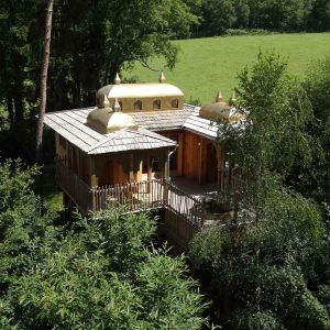 Cabane perchée en Aquitaine, avec un toit doré et entourée de verdure.