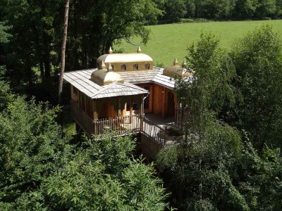 Cabane perchée en Aquitaine, avec un toit doré et entourée de verdure.