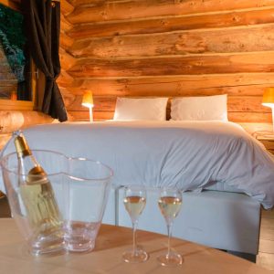Chalet en bois chaleureux avec lit douillet et bouteille de champagne sur la table.