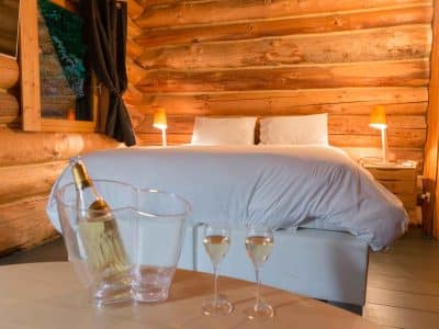 Chalet en bois chaleureux avec lit douillet et bouteille de champagne sur la table.