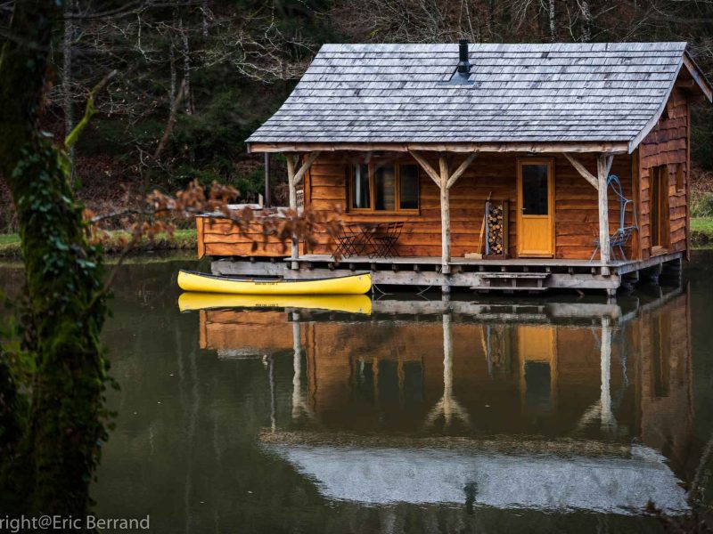 Cabane flottante en bois sur un lac, avec un canoë jaune à lavant.