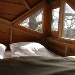 Cabane perchée en bois avec vue sur la nature, lit douillet à lintérieur.