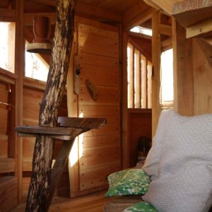 Cabane en bois dans les arbres, intérieur chaleureux avec coussins colorés.