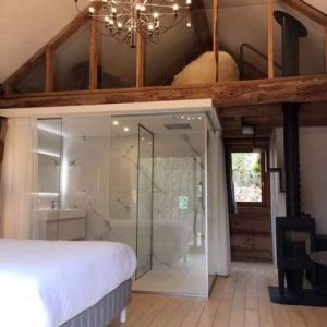 Hébergement insolite en Aquitaine : chambre moderne avec salle de bain vitrée et poutres apparentes.