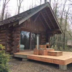 Cabane en bois au cœur de la forêt, avec terrasse et spa extérieur.