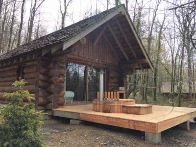 Cabane en bois au cœur de la forêt, avec terrasse et spa extérieur.