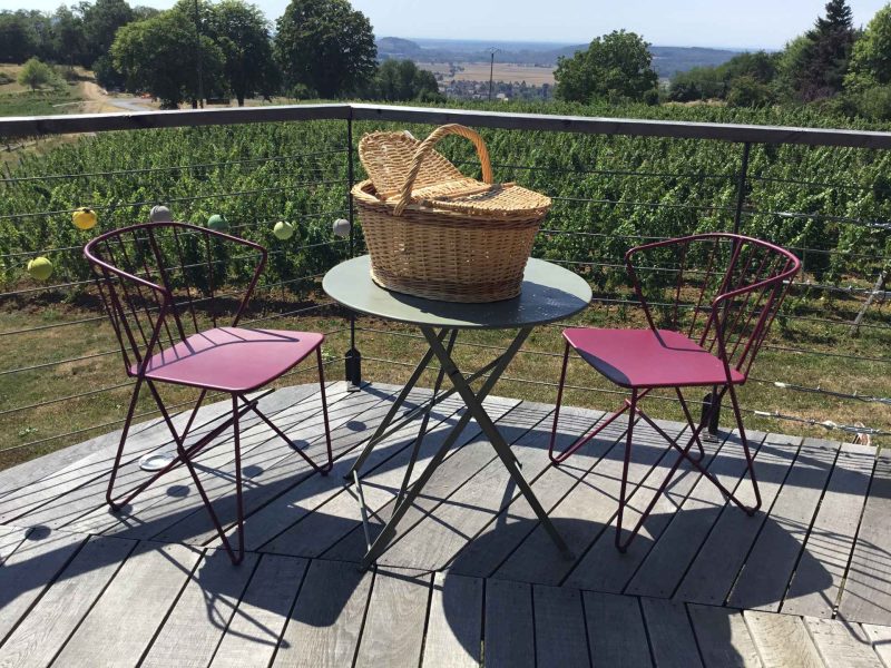 Terrasse dun gîte avec vue sur les vignes, table et chaises colorées.