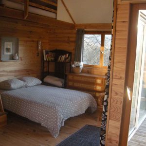 Chalet en bois avec lit douillet et grandes fenêtres sur la nature en Bourgogne.