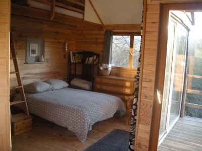 Chalet en bois avec lit douillet et grandes fenêtres sur la nature en Bourgogne.