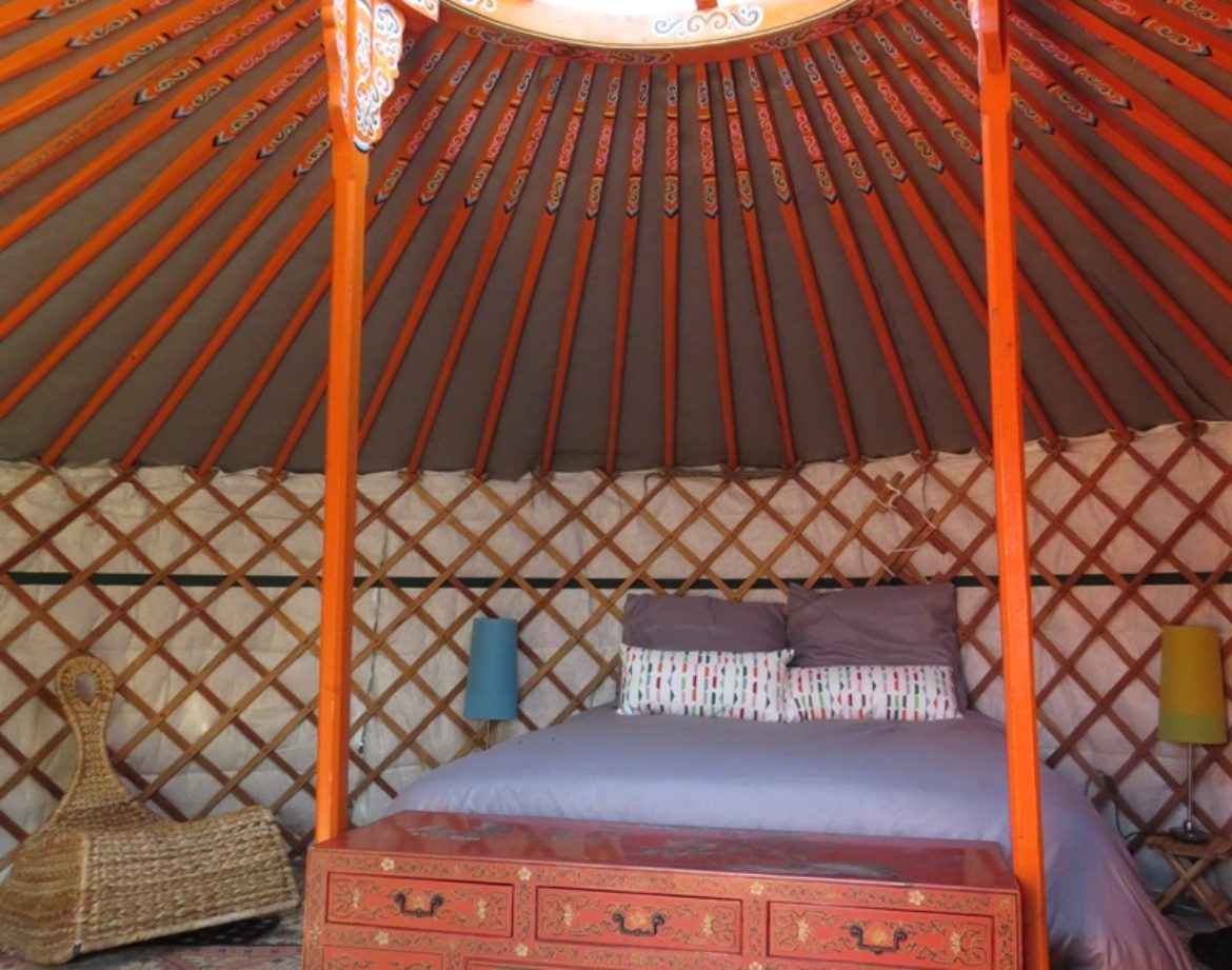 Yourte colorée en Bourgogne, avec un lit central et un plafond en bois décoratif.