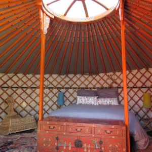 Yourte colorée en Bourgogne, avec un lit central et un plafond en bois décoratif.