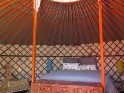 Yourte colorée en Bourgogne, avec un lit central et un plafond en bois décoratif.