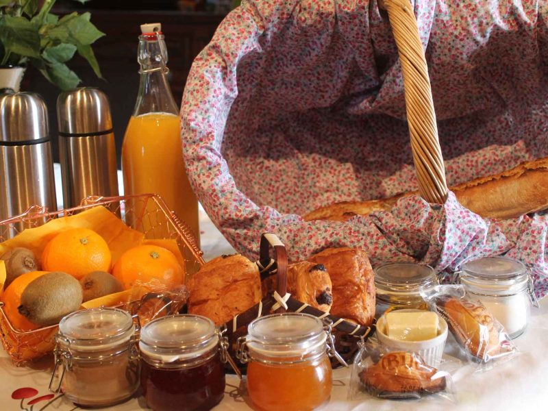 Panier de petit-déjeuner dans un gîte, avec fruits, viennoiseries et confitures.