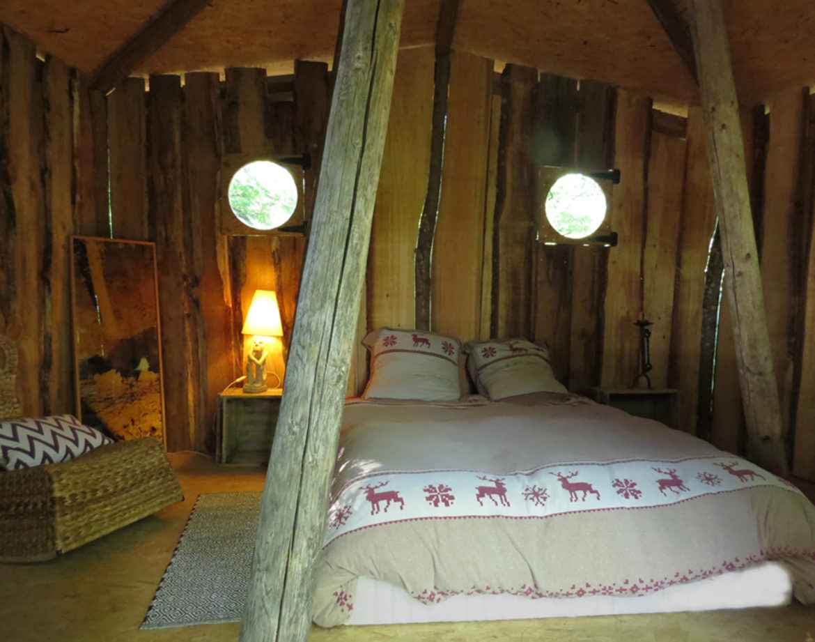 Cabane en bois en Bourgogne, lit douillet avec lumière douce et fenêtres rondes.