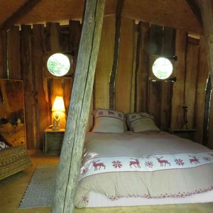 Cabane en bois en Bourgogne, lit douillet avec lumière douce et fenêtres rondes.