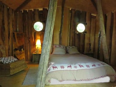 Cabane en bois en Bourgogne, lit douillet avec lumière douce et fenêtres rondes.