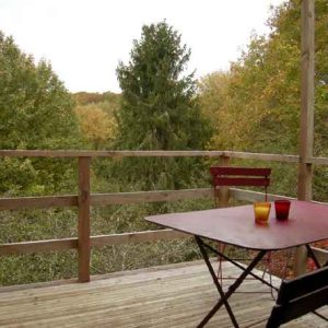 Cabane perchée en Bourgogne avec une terrasse surplombant la forêt verdoyante.