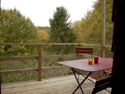 Cabane perchée en Bourgogne avec une terrasse surplombant la forêt verdoyante.