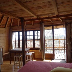 Cabane en bois avec vue panoramique, lit confortable et table en bois.