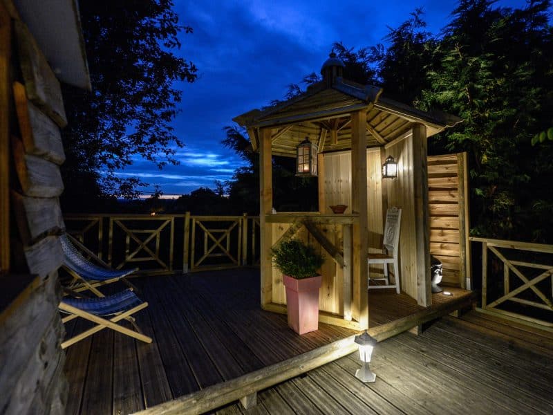 Cabane en bois avec terrasse éclairée, offrant une vue nocturne apaisante.