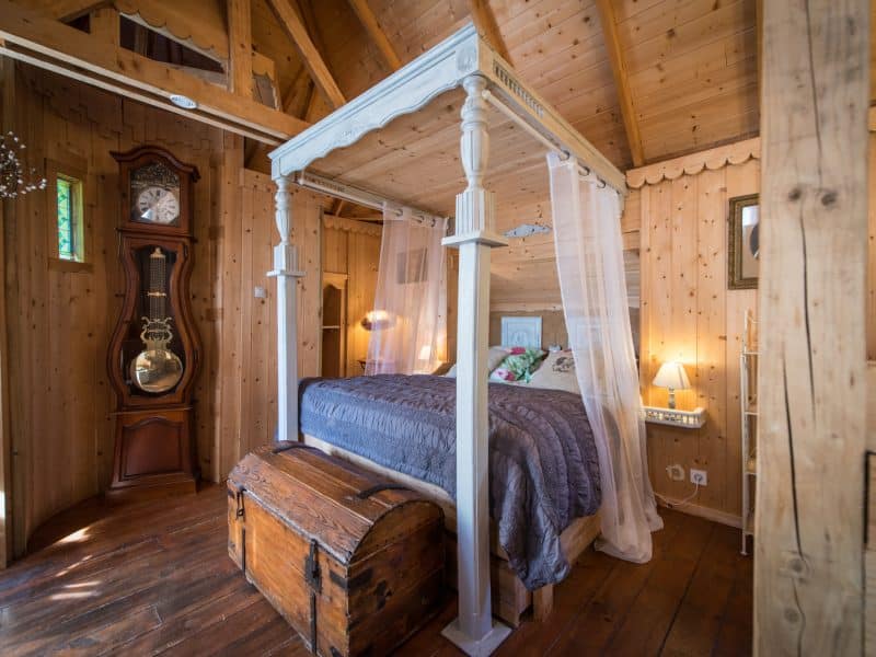 Chalet en bois avec lit à baldaquin et coffre ancien, ambiance chaleureuse et cosy.