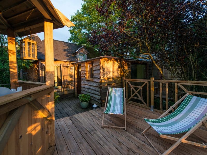 Cabane en bois avec terrasse ensoleillée et chaises longues confortables.