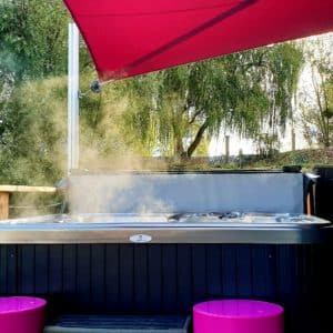 Bungalow avec jacuzzi sur terrasse, entouré de verdure et dun parasol rose.