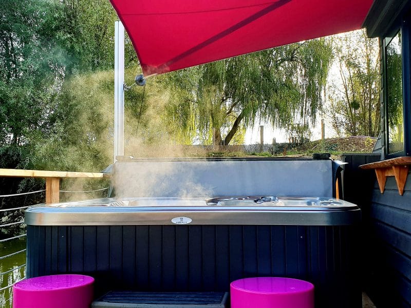 Bungalow avec jacuzzi sur terrasse, entouré de verdure et dun parasol rose.