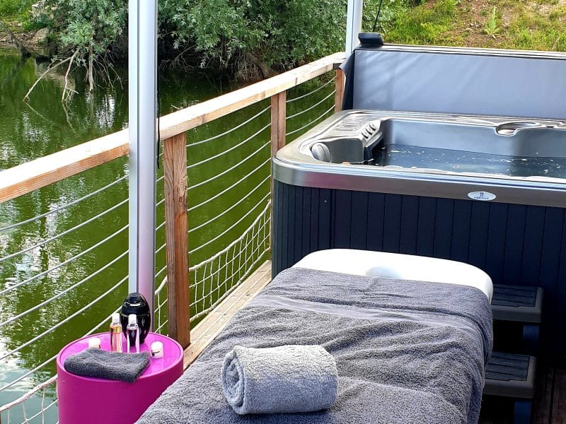 Hébergement flottant avec spa, terrasse en bois et vue sur la rivière.