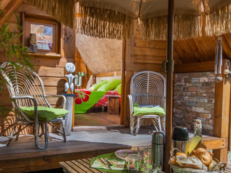 Chalet en bois avec terrasse ombragée et table décorée pour un petit déjeuner.
