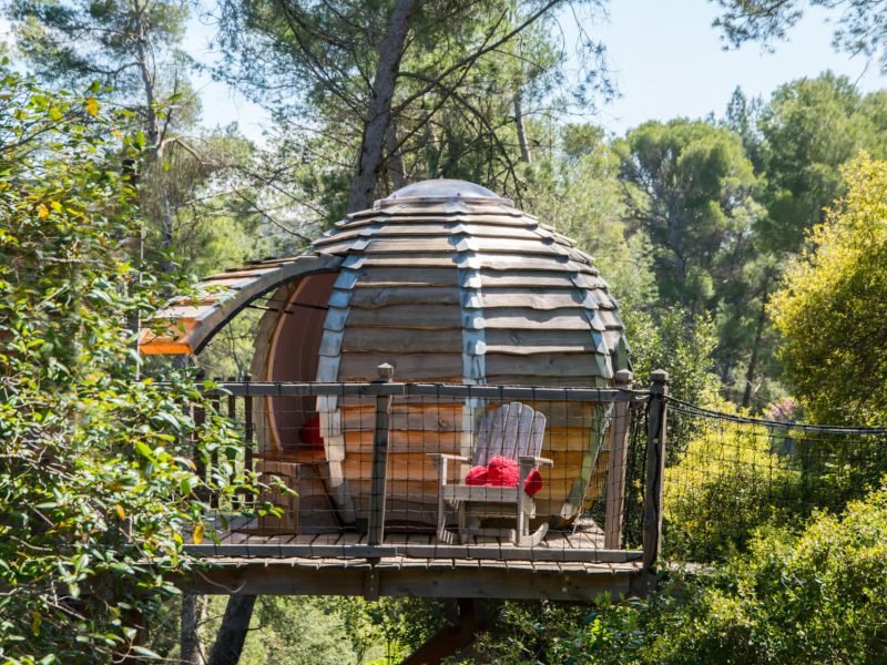Cabane dans les arbres avec un balcon, entourée de verdure apaisante.