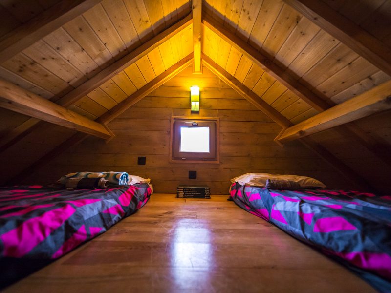 Chalet en bois avec lits simples, ambiance chaleureuse et lumière douce.